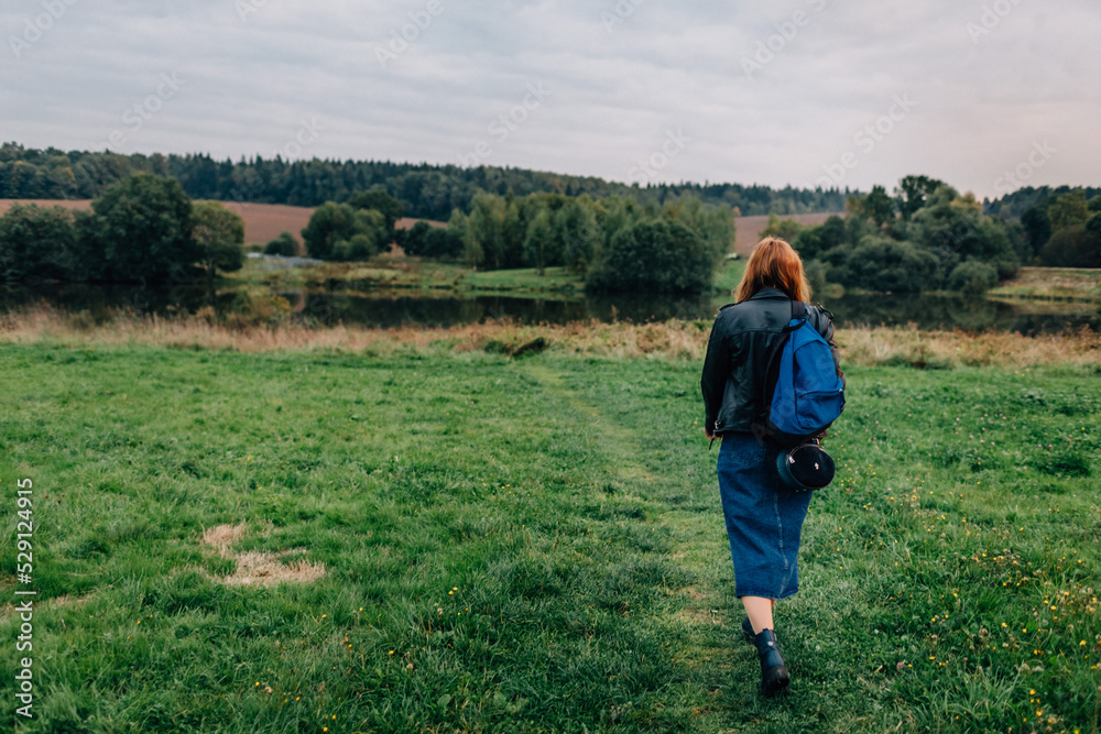 Young woman walking outdoors in green autumn field in evening. Woman with a backpack hiking outdoors