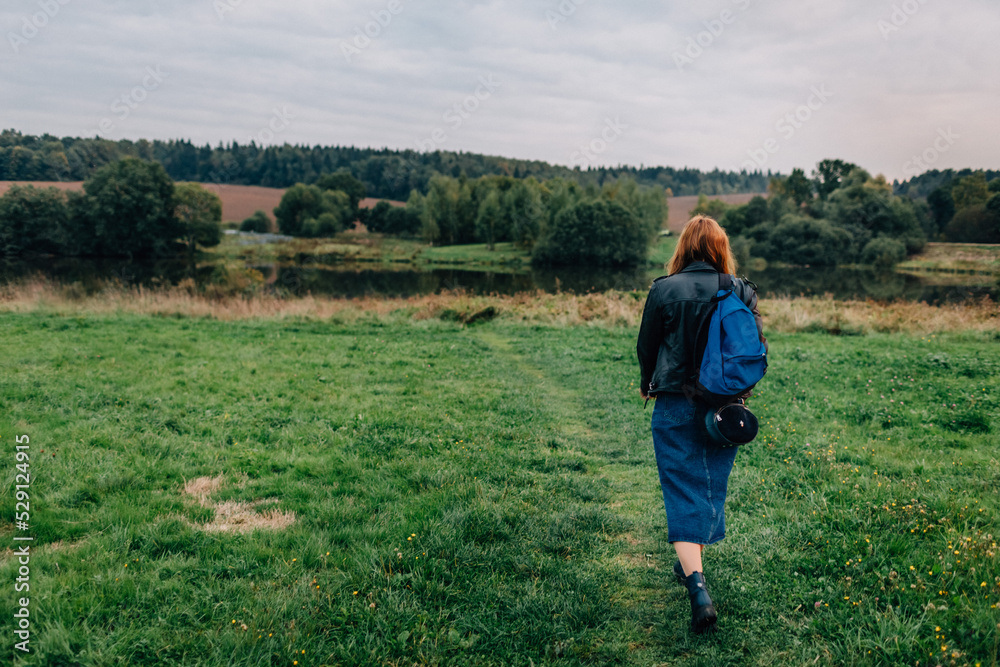 Young woman walking outdoors in green autumn field in evening. Woman with a backpack hiking outdoors Young woman walking outdoors in green autumn field in evening. Woman with a backpack hiking outdoors