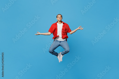 Full body young man of African American ethnicity wear red shirt jump high hold spread hands in yoga om aum gesture relax meditate try to calm down isolated on plain pastel light blue cyan background.