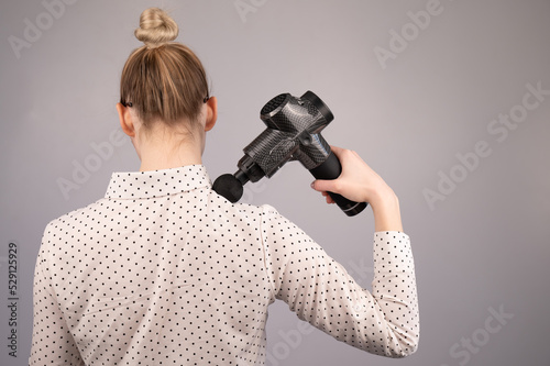 Photography Caucasian business lady makes herself a back massage with a massager gun on a white background
