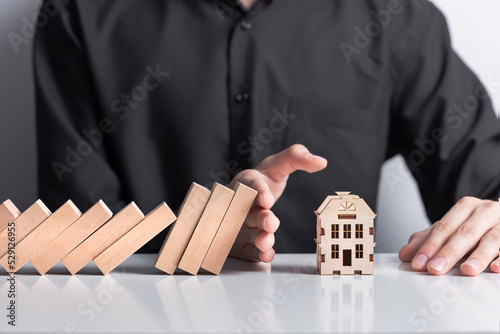 hand stops falling wooden dominoes falling on house model, real estate protection, home insurance, risk insurance concept, domino principle