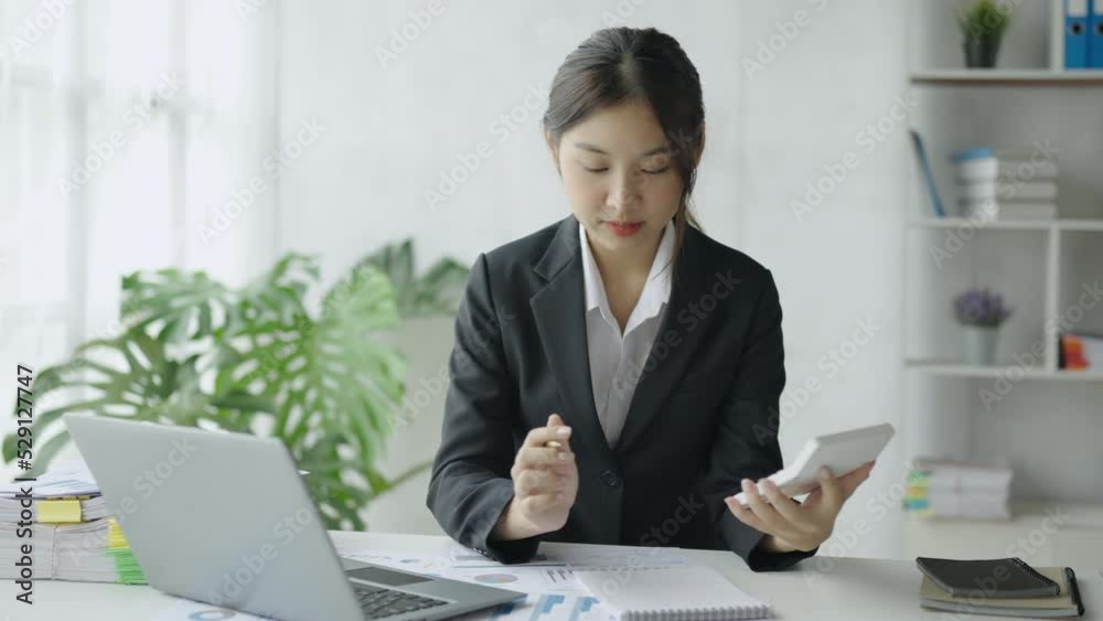 Young Asian businesswoman using a calculator to calculate business principles. Accounting statistics concept at the office.