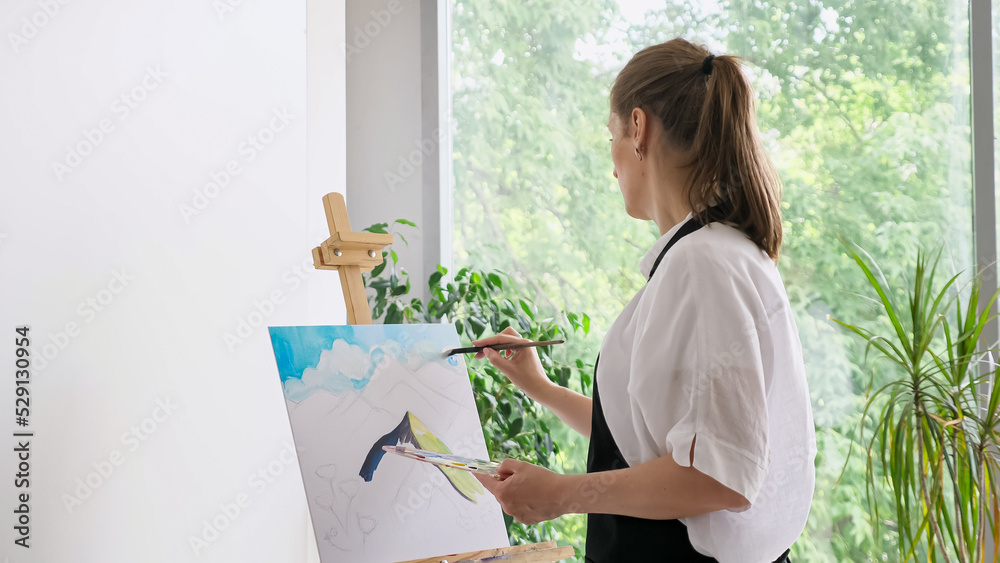 Mature woman paints sky watercolor on canvas with paintbrush. Skilled female artist enjoys painting on wooden easel in comfortable atmosphere closeup Mature woman paints sky watercolor on canvas with paintbrush. Skilled female artist enjoys painting on wooden easel in comfortable atmosphere closeup