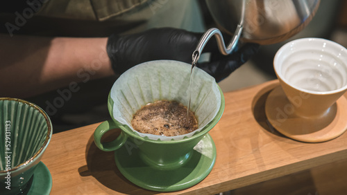 Close up to the barista's hand to make coffee by using the kettle to pour hot water over the coffee powder.