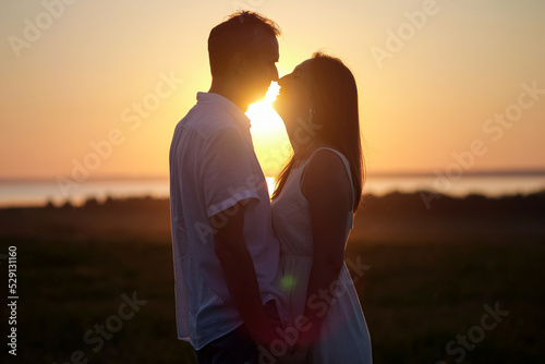Husband expresses true love to gorgeous wife at back sunset. Couple silhouettes look at each other with lovely smile and enjoy landscape together closeup