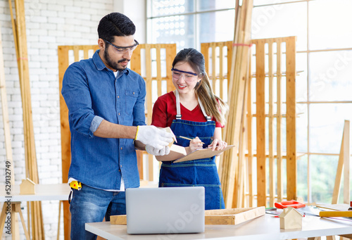 Asian Indian professional male and female engineer architect foreman labor worker lover couple wear safety goggles standing cuddling leaning together holding wooden home model in construction site