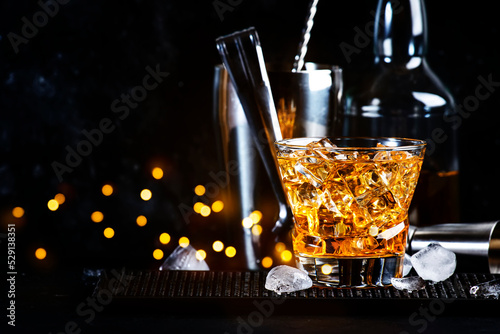 Godfather cocktail with scotch whiskey, almond amaretto liqueur and ice cubes.. Black background, steel bar tools photo