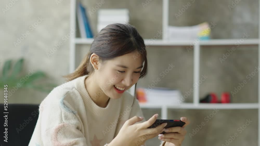 Beautiful and cute young Asian woman sitting on sofa and using smartphone happily and play game at her home. Beautiful and cute young Asian woman sitting on sofa and using smartphone happily and play game at her home.