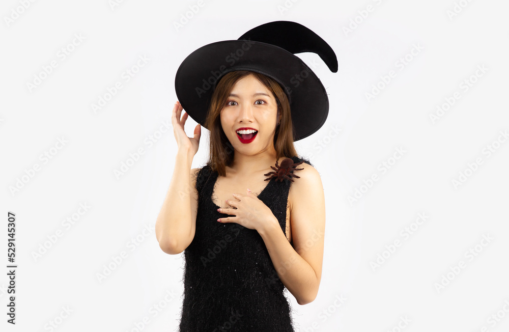 Halloween theme, young pretty asian woman in black dress wearing witch hat posing surprised and wow on white background. Halloween theme, young pretty asian woman in black dress wearing witch hat posing surprised and wow on white background.