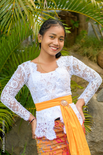 Fotografie Pretty smiling Balinese girl in traditional orange and white suit among tropical leaves