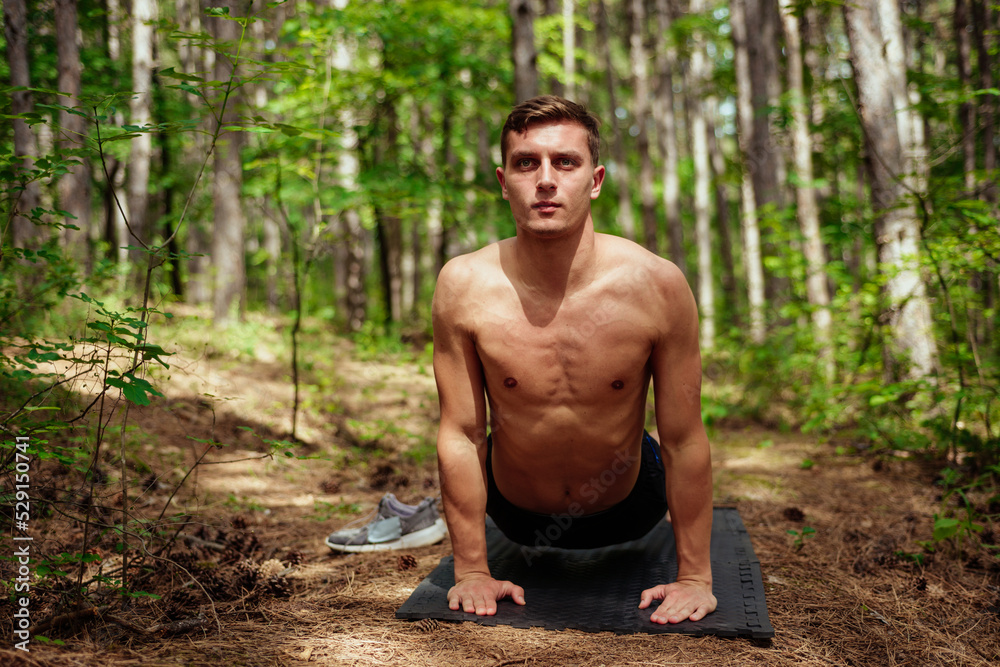 Young man with perfectly prominent muscles doing exercises in the park