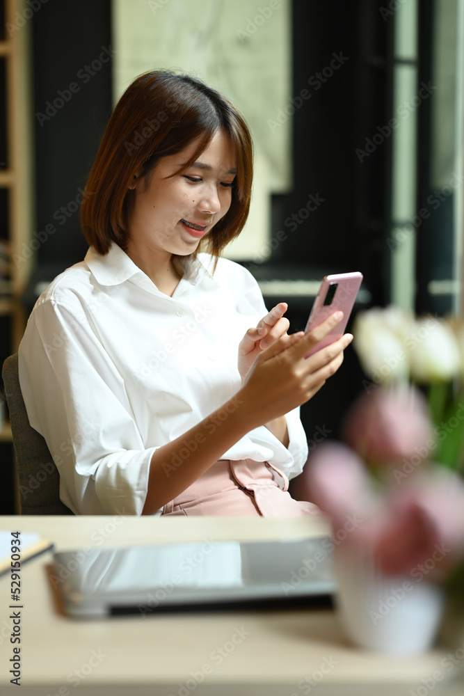 Charming young asian woman using smart phone sitting in bright modern corporate office Charming young asian woman using smart phone sitting in bright modern corporate office