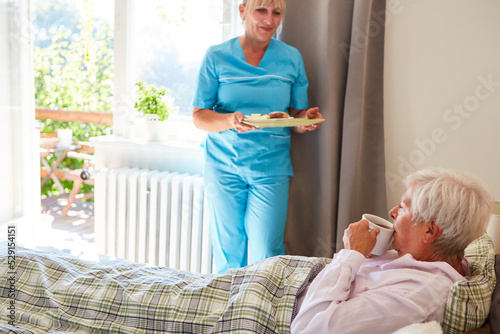 Altenpflegerin bringt einer Seniorin das Frühstück ans Bett