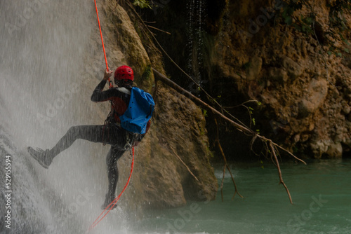 Unrecognizable man with helmet, neoprene dress and harness practicing rappelling in a waterfall