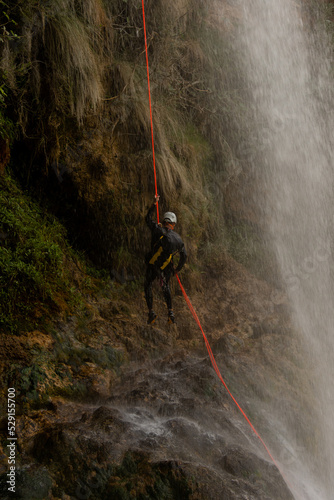 Man wearing a helmet and wetsuit finishing a rappel down a waterfall