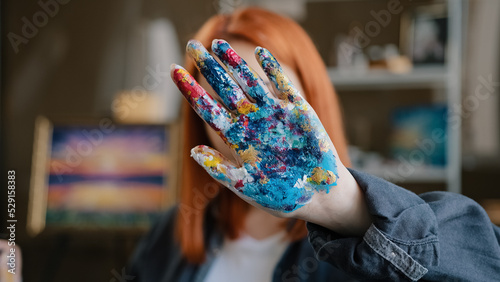 Female calm red-haired girl artist lady Caucasian 30s woman painter designer holding hand in front stop gesture not no gesture showing dirty in acrylic paint palms looking at camera in art studio