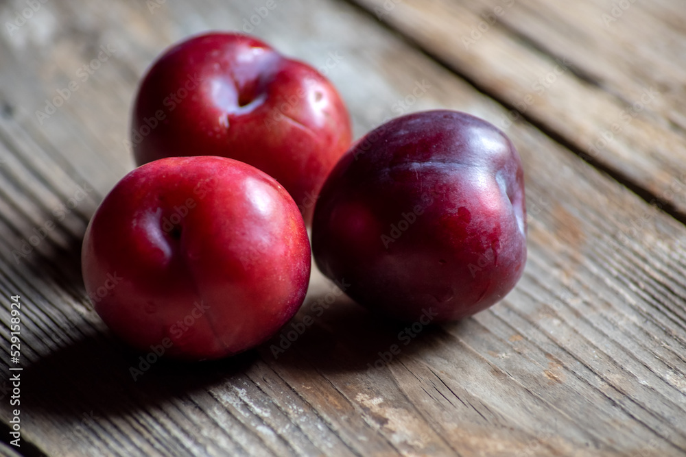 Close-up of three ripe plums on rustic wood Close-up of three ripe plums on rustic wood