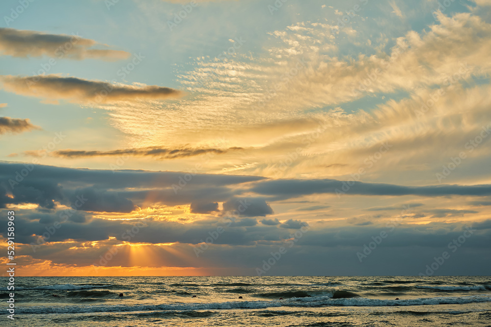 Sunset sky over the sea, late evening with colorful clouds of orange sunlight, the rays of the sun shine through the clouds
