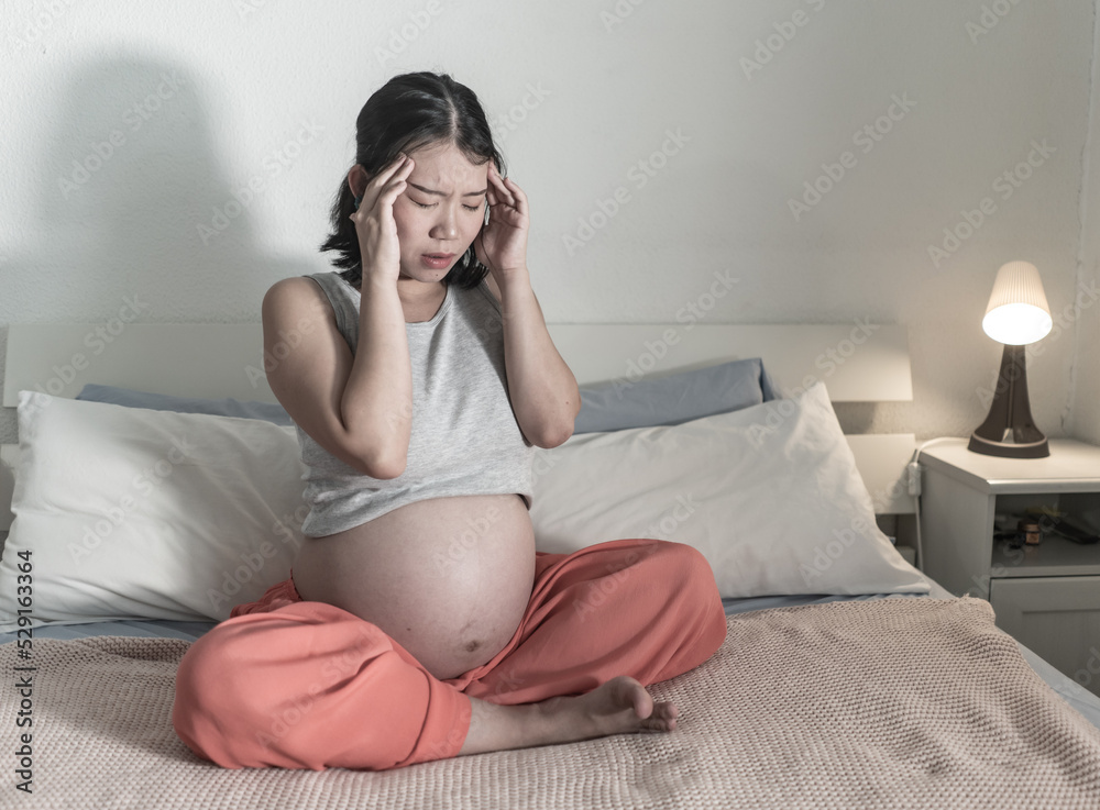 home portrait of young tired and depressed Asian Chinese woman pregnant in bed having nausea and feeling unwell suffering headache and pregnancy body pain home portrait of young tired and depressed Asian Chinese woman pregnant in bed having nausea and feeling unwell suffering headache and pregnancy body pain
