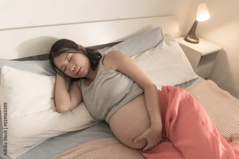 home portrait of young tired and depressed Asian Korean woman pregnant in bed having nausea and feeling unwell suffering pregnancy body pain and fatigue home portrait of young tired and depressed Asian Korean woman pregnant in bed having nausea and feeling unwell suffering pregnancy body pain and fatigue