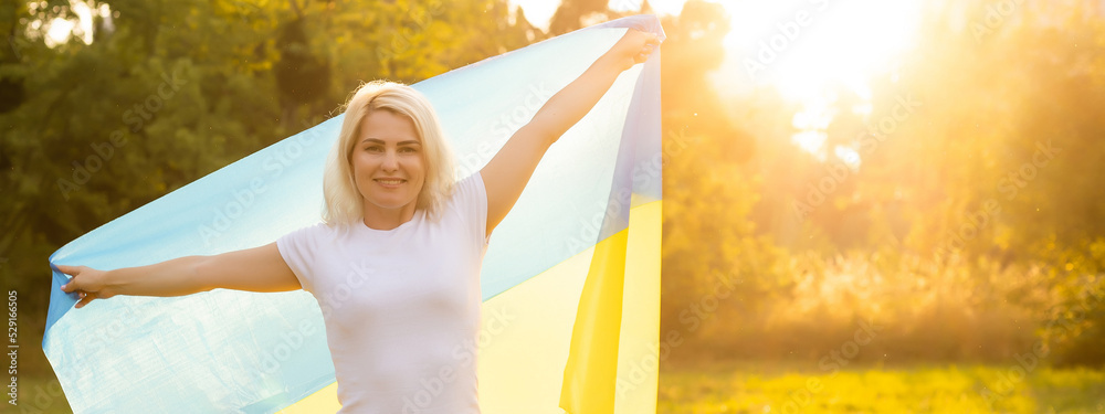 Fototapeta premium Girl carries fluttering blue and yellow flag of Ukraine in field. Ukraine's Independence Flag Day. Constitution day. Woman in traditional embroidery with flag of Ukraine. 24 August. Patriotic holiday.