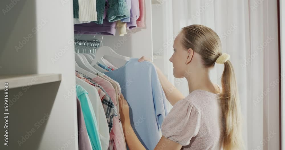 A teenager chooses a dress in the dressing room. Low angle shot A teenager chooses a dress in the dressing room. Low angle shot