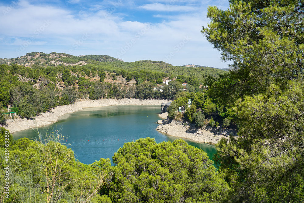 Spectacular panoramic views of the Guadalhorce reservoir, next to the Caminito del Rey in Malaga, Spain. Turquoise blue water and forest with blue sky on a sunny day.