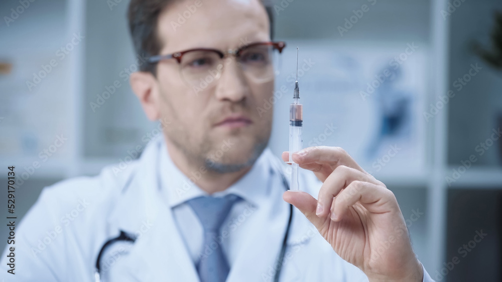 serious doctor in white coat and glasses holding syringe in clinic. serious doctor in white coat and glasses holding syringe in clinic.