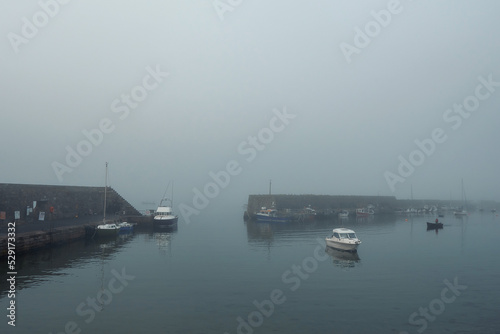 Small boat in a harbor morning fog in the background. Cool tone and mood. Transportation and travel theme.