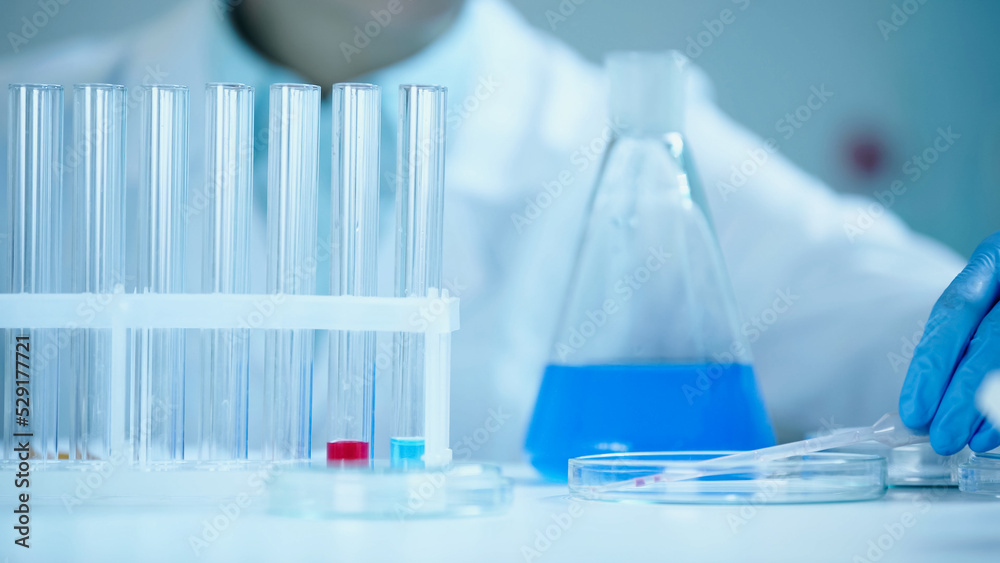 partial view of blurred scientist in latex glove taking pipette on petri dish in laboratory. partial view of blurred scientist in latex glove taking pipette on petri dish in laboratory.