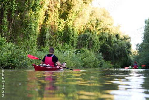 Rear view of man kayaking on red kayak in the summer river near green trees