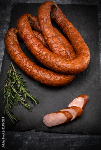 Smoked sausage in rings on black stone background. Composition with traditional Polish meat cold cuts and fresh herbs.