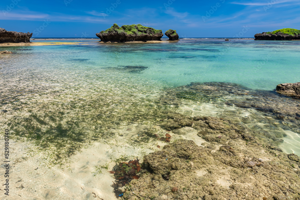 Crystal clear turquoise sea waters forming natural pools between coral rocks, blue sky.