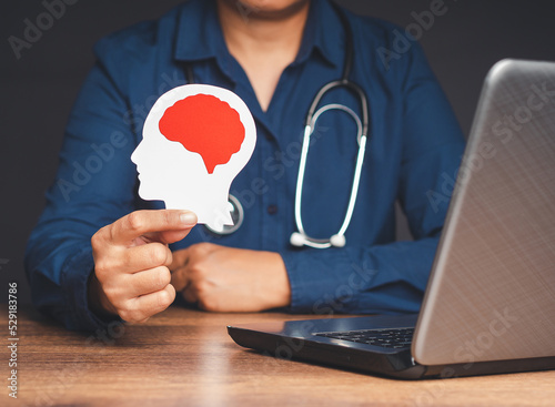 Doctor holding a white head made from paper with a red brain symbol while sitting in the hospital