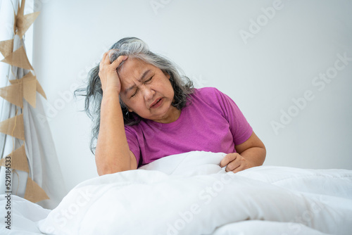 Unhealthy elderly senior Asian woman sitting on bed suffering from headache and migraine so pain and illness, Stress senior woman sit on bed at home alone, tried, Unhappy Elderly despond concept
