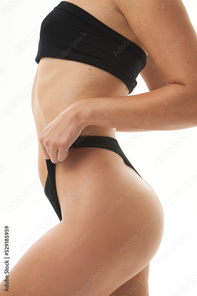 Fototapeta premium A woman with a sexy back, a narrow big ass in underwear. Beautiful female body in shape. Closeup healthy girl with toned slim body, soft skin and elastic buttocks, thighs in black bikini panties.