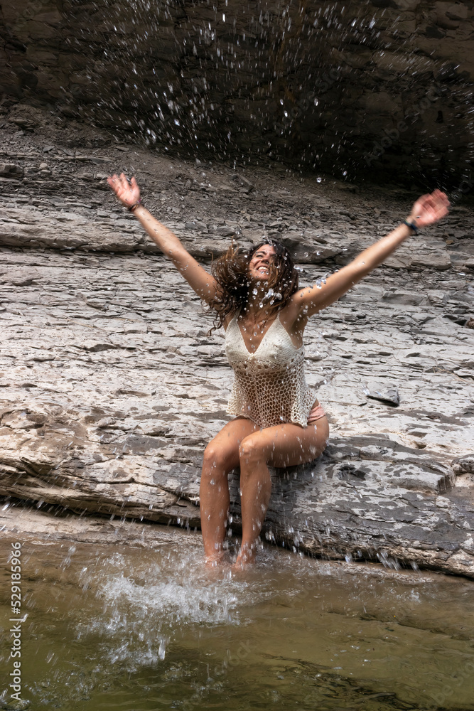 Fototapeta premium Young beautiful woman splashing water in a river sitting on some rocks