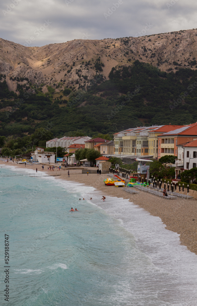 Beach of Baska, Krk, Croatia, on a cloudy day with mountains (vertical)
