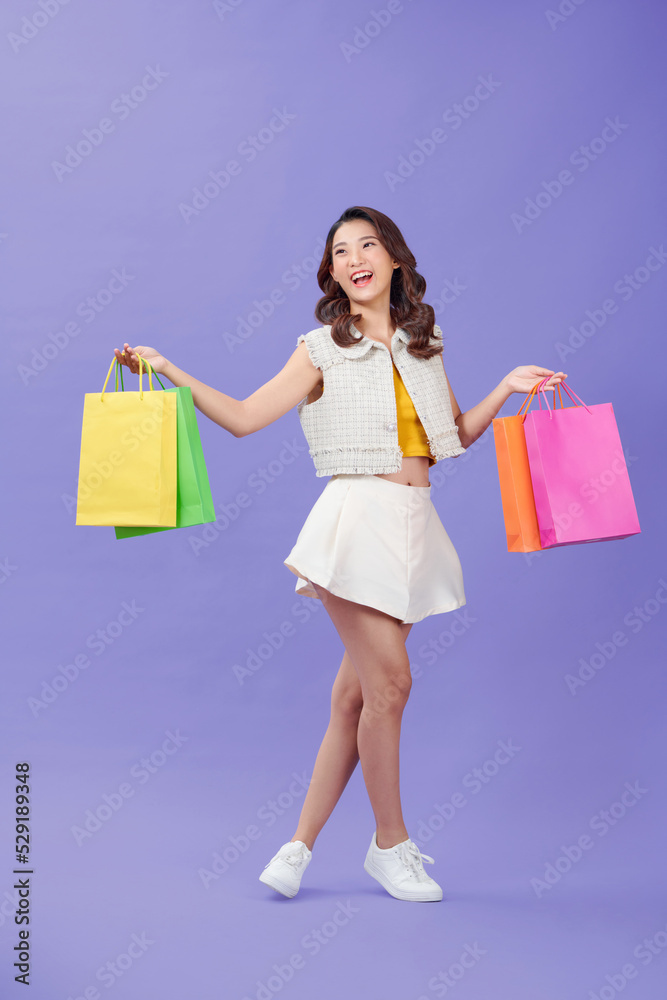 Happy young woman with color shopping bags, over purple background