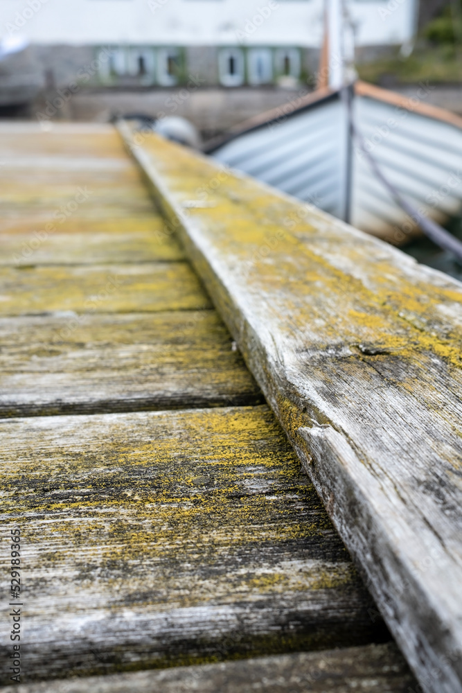 Old weathered wooden pier and a moored sailboat in the background, out of focus.