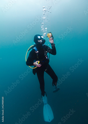 A scuba diver is underwater at a safety stop holding onto the reel of her surface marker buoy