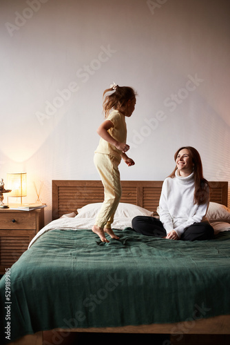 Little caucasian girl have fun with mother. Jumping on bed christmas morning. Happy family christmas concept
