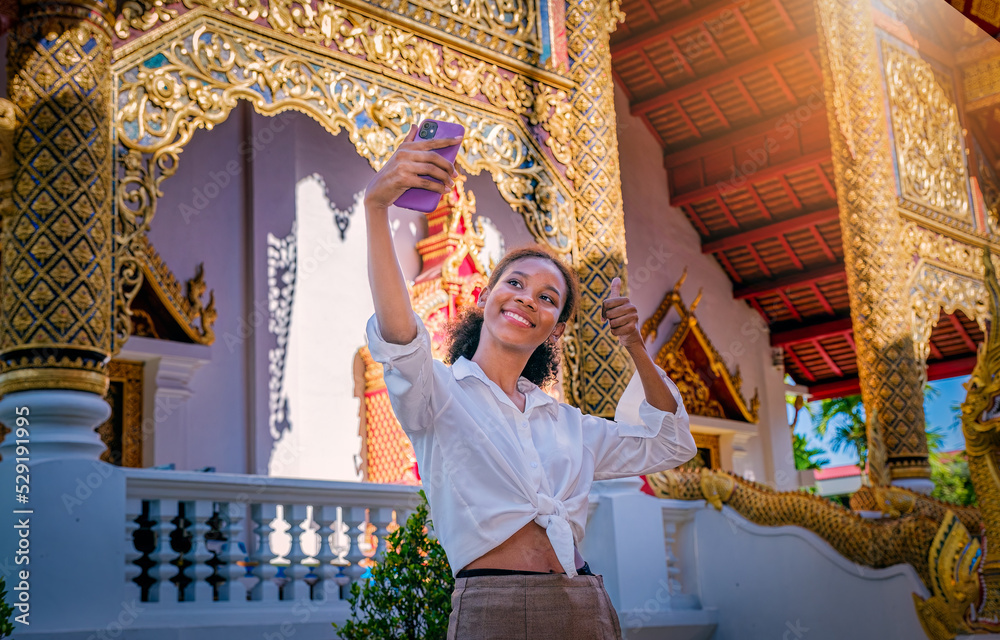 Young smiling girl tourist enjoy visiting and taking selfy in a Thai temple in Chiang Mai, Thailand. Travel concept.