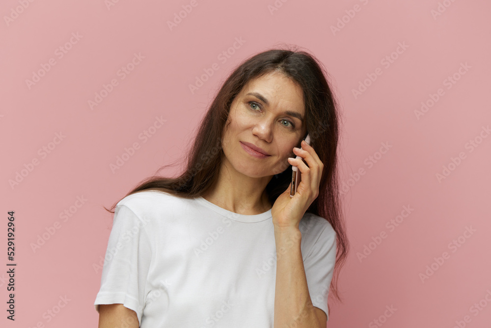 portrait of a beautiful, cute, attractive brunette woman in a light t-shirt standing on a pink background and talking on the phone, with a pleasant smile on her face portrait of a beautiful, cute, attractive brunette woman in a light t-shirt standing on a pink background and talking on the phone, with a pleasant smile on her face