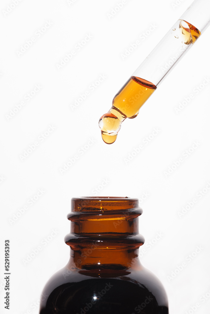 A drop of liquid falling from a pipette into an amber bottle. Skincare products, natural cosmetic on white background. Beauty concept for face and body care. A drop of liquid falling from a pipette into an amber bottle. Skincare products, natural cosmetic on white background. Beauty concept for face and body care.
