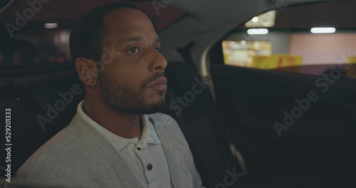 Fotobehang A black man seated in car backseat commuting from work at night
