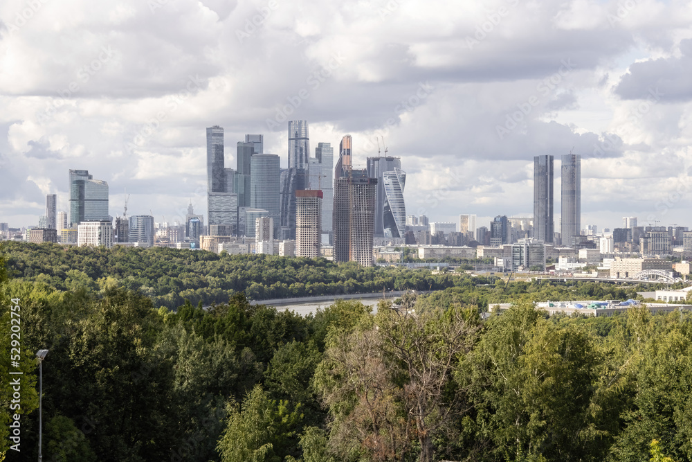 Parks with trees and bushes, new business district Moscow City with skyscrapers, Moscow river, panorama of Moscow, capital of Russia. Cloudy sky on a summer day.