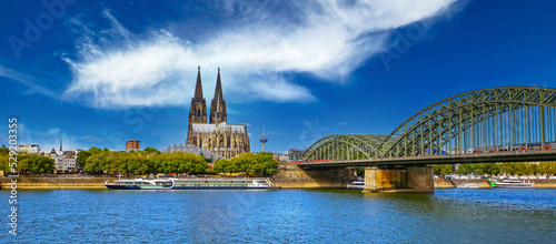 Beautiful river rhine river skyline, medieval gothic dome, Hohenzollern bridge, dramit blue summer sky - Cologne, Germany (focus on center of upper bridge) photo