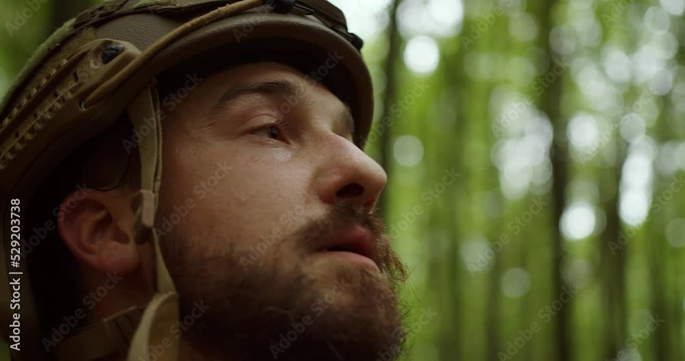 a bearded soldier in a helmet looks up against the background of green trees in the forest. close-up of the face. sweaty face a bearded soldier in a helmet looks up against the background of green trees in the forest. close-up of the face. sweaty face