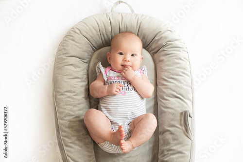 Cute caucasian newborn baby girl in the baby nest playing with her feet. baby milestones